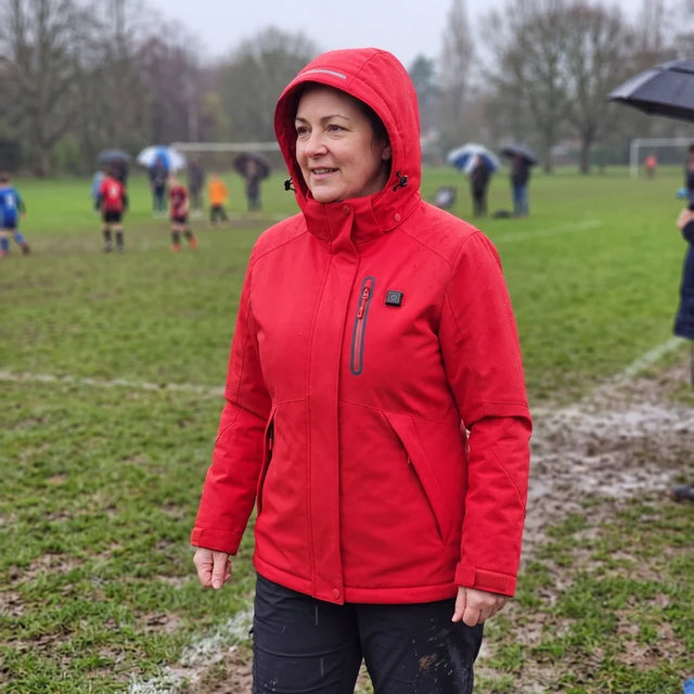 Woman in a red Expedition 14 heated parka beside a soccer field in the rain